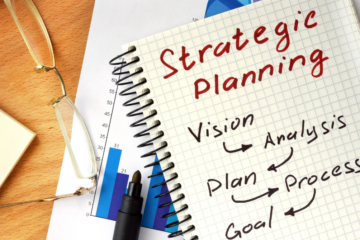 background image of notebook on desk with pens and other paper. written on notepad are the words Strategic Planning
