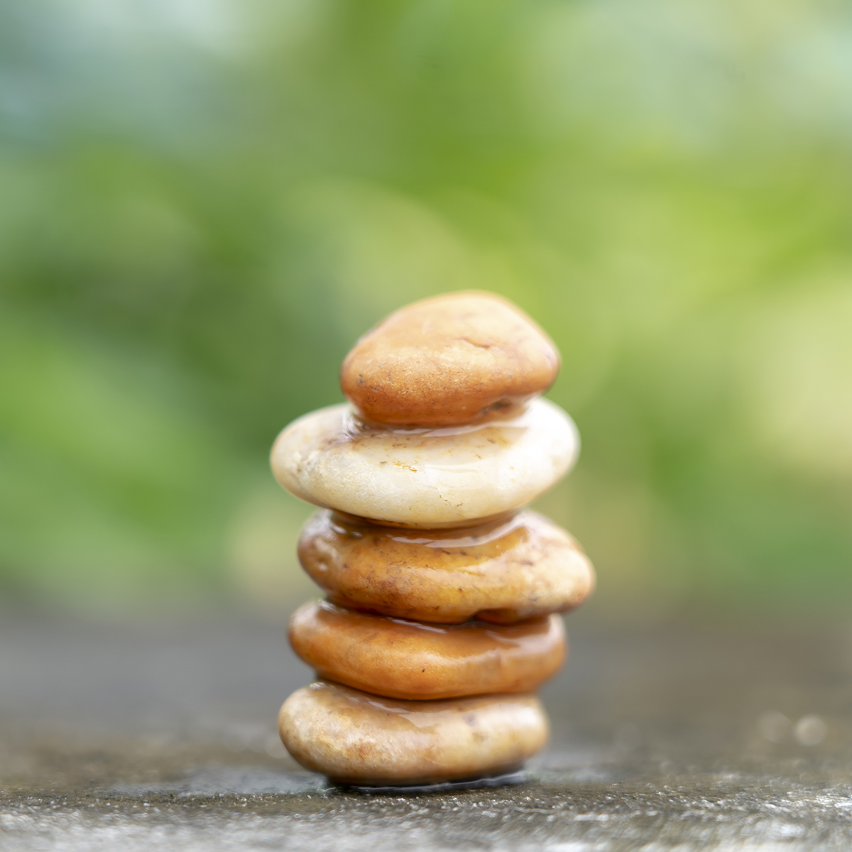 Meditation stones with rain drop water on cement floor on green nature background. Pyramid pebbles free space. Calm, buddhism symbol or aromatherapy set concept.