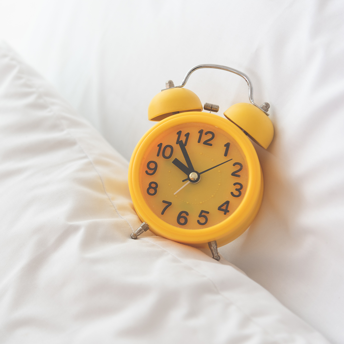 Yellow alarm clock on white bed background. Travel and Vacation concept. Home object accessories theme.
