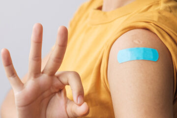 woman showing OK sign with bandage after receiving covid 19 vaccine. Vaccination, herd immunity, side effect, booster dose, vaccine passport and Coronavirus pandemic