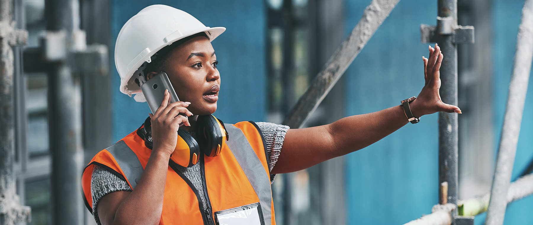Shot of a young woman talking on a cellphone while working at a construction site