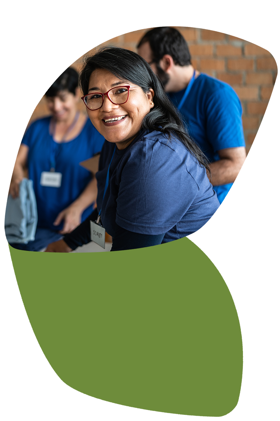 Woman in foreground smiling at camera while out of focus people sort clothing items in background.