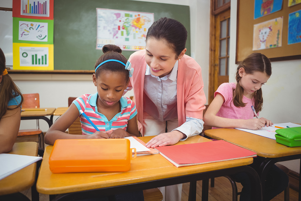 Pupil and teacher at desk in classroom at the elementary school