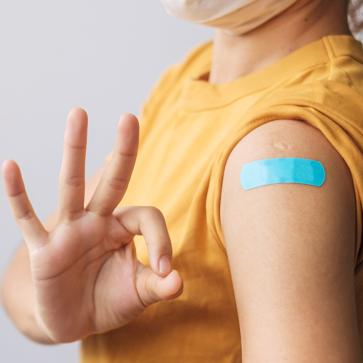 woman showing OK sign with bandage after receiving covid 19 vaccine. Vaccination, herd immunity, side effect, booster dose, vaccine passport and Coronavirus pandemic